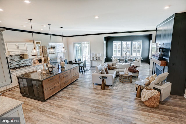 kitchen featuring light wood-type flooring, stainless steel gas cooktop, white cabinetry, decorative light fixtures, and dark stone countertops