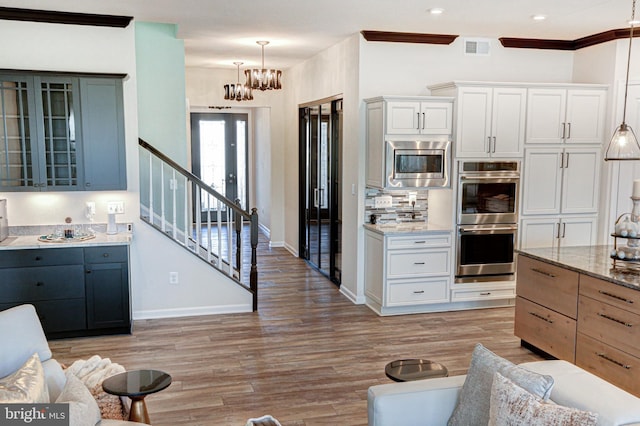 kitchen featuring white cabinets, stainless steel appliances, hanging light fixtures, and light stone counters