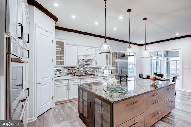 kitchen with white cabinets, a kitchen island with sink, decorative light fixtures, and light stone counters