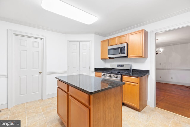 kitchen with ornamental molding, a kitchen island, appliances with stainless steel finishes, dark stone countertops, and light hardwood / wood-style floors