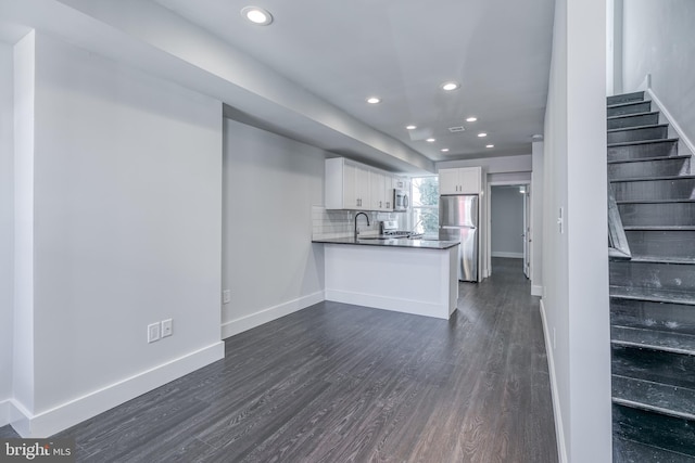 kitchen with decorative backsplash, dark hardwood / wood-style floors, kitchen peninsula, white cabinetry, and appliances with stainless steel finishes