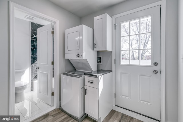 laundry area with cabinets, light wood-type flooring, and stacked washer and dryer