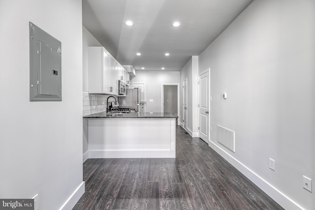 kitchen featuring electric panel, kitchen peninsula, white cabinetry, stainless steel appliances, and dark stone counters