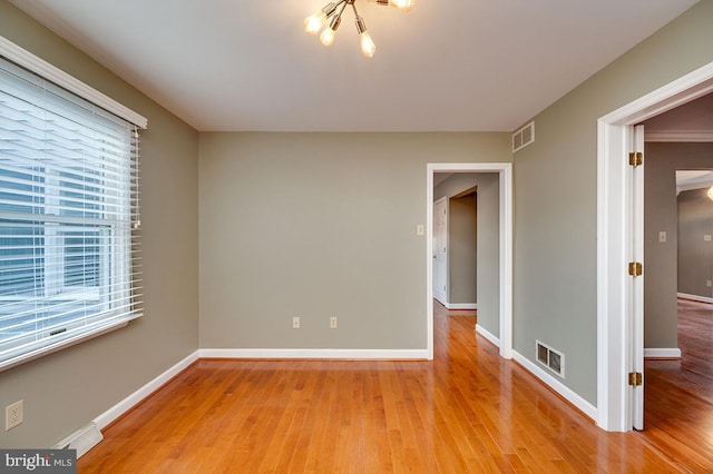 spare room with hardwood / wood-style floors and an inviting chandelier