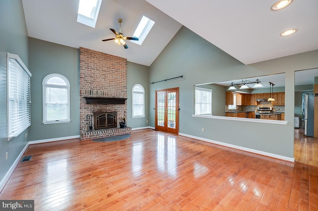 unfurnished living room with a skylight, light hardwood / wood-style flooring, high vaulted ceiling, and a healthy amount of sunlight