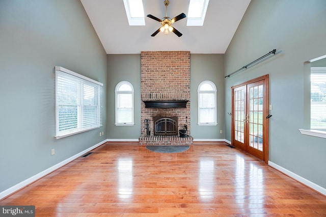 unfurnished living room featuring a skylight, a brick fireplace, plenty of natural light, and light hardwood / wood-style floors