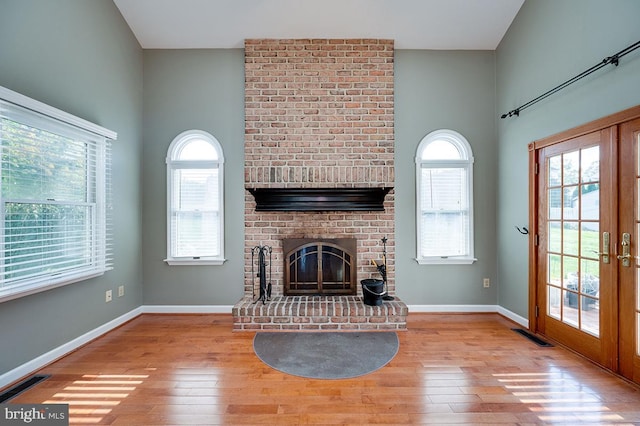 unfurnished living room featuring french doors, light wood-type flooring, and a brick fireplace