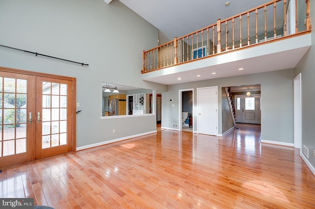 unfurnished living room with french doors, light hardwood / wood-style floors, high vaulted ceiling, and a healthy amount of sunlight