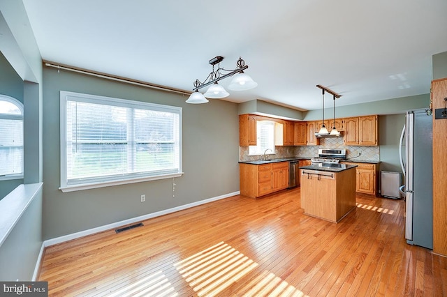 kitchen featuring a kitchen island, decorative backsplash, pendant lighting, light hardwood / wood-style flooring, and appliances with stainless steel finishes