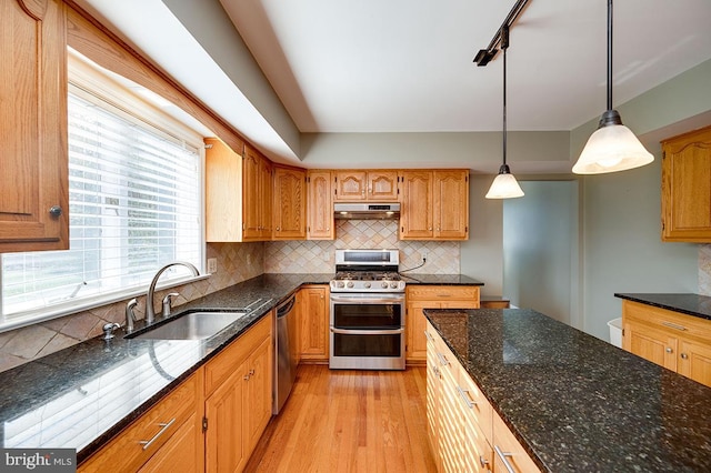 kitchen featuring light hardwood / wood-style floors, dark stone counters, sink, stainless steel appliances, and hanging light fixtures