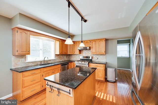 kitchen featuring plenty of natural light, a kitchen island, sink, stainless steel appliances, and hanging light fixtures