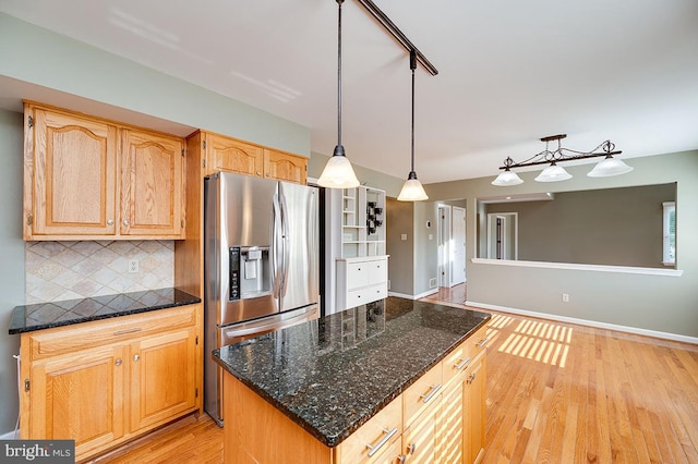 kitchen with hanging light fixtures, light hardwood / wood-style flooring, stainless steel fridge with ice dispenser, dark stone counters, and decorative backsplash