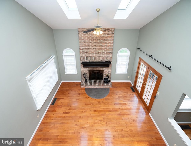 unfurnished living room featuring a skylight, a fireplace, ceiling fan, and light hardwood / wood-style floors