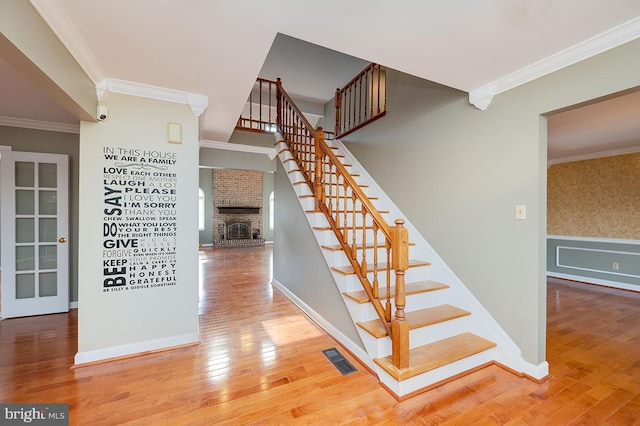 stairway featuring hardwood / wood-style flooring, crown molding, and a fireplace