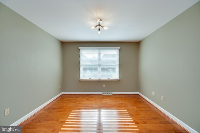 spare room featuring a notable chandelier and light hardwood / wood-style flooring