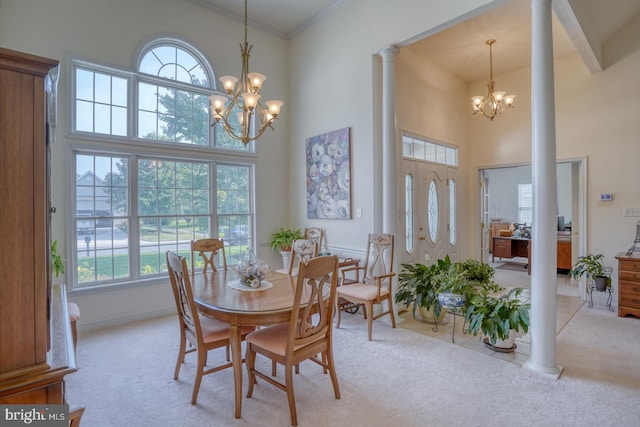 carpeted dining room with a towering ceiling, a chandelier, crown molding, and decorative columns