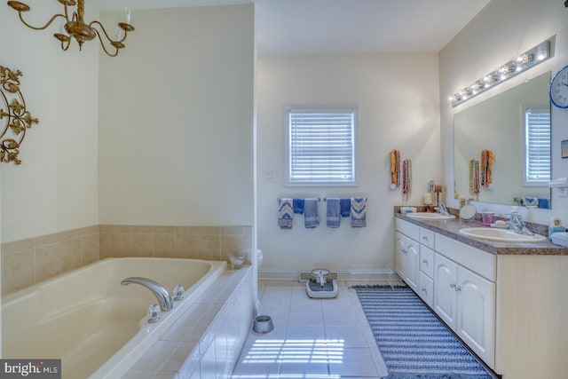 bathroom featuring tile patterned flooring, vanity, a notable chandelier, and tiled tub