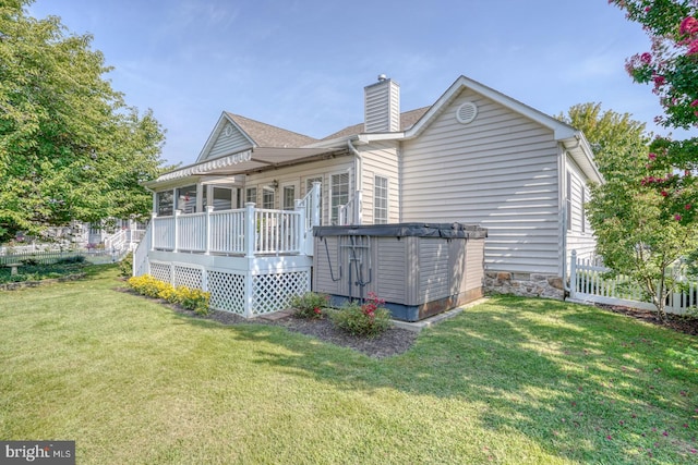 rear view of property with a hot tub, a wooden deck, and a lawn