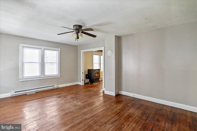 unfurnished room featuring ceiling fan, dark hardwood / wood-style floors, a wood stove, and a baseboard radiator