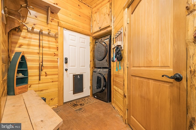 clothes washing area featuring wooden walls and stacked washer and dryer