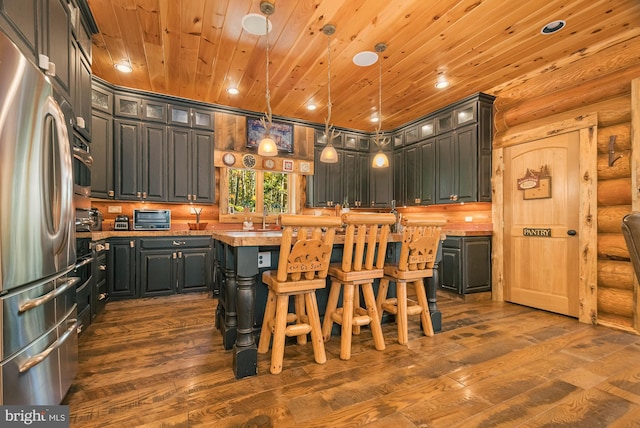 kitchen with dark hardwood / wood-style floors, a kitchen island, log walls, and stainless steel refrigerator