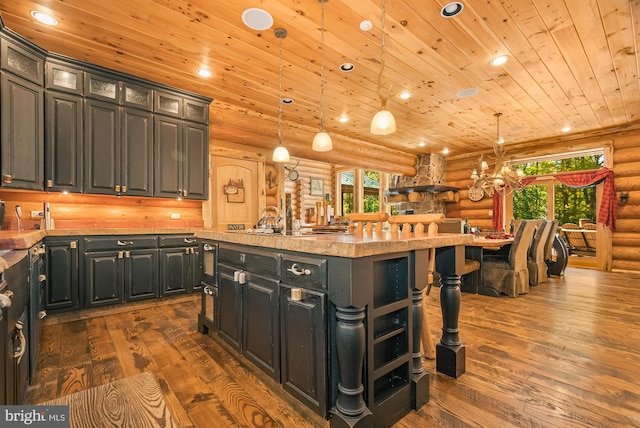 kitchen with an island with sink, wood ceiling, rustic walls, hanging light fixtures, and dark hardwood / wood-style floors