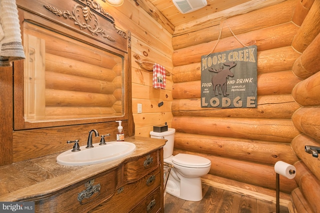 bathroom featuring vanity, rustic walls, hardwood / wood-style flooring, and toilet