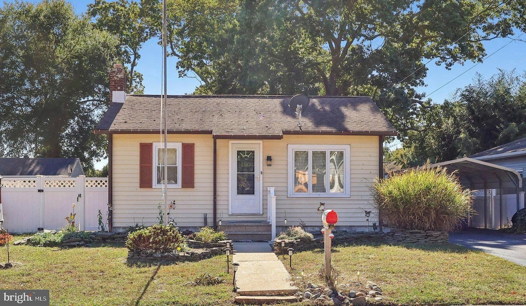 bungalow-style house with a detached carport, a front lawn, and fence