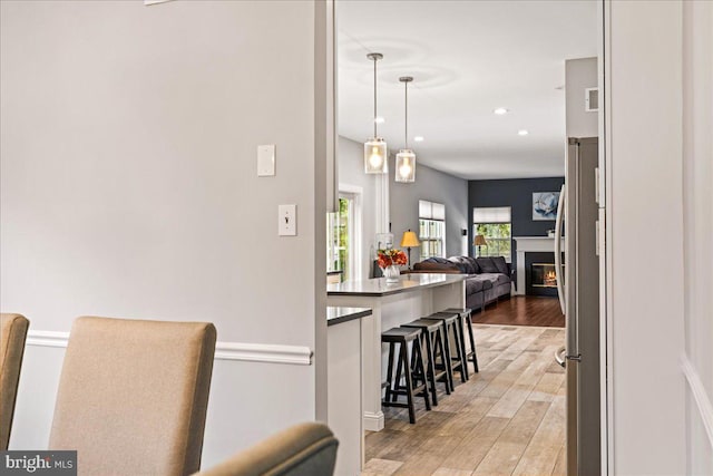 kitchen with stainless steel fridge, hardwood / wood-style floors, decorative light fixtures, and a kitchen bar