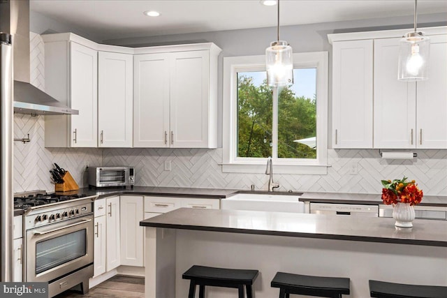 kitchen with a breakfast bar area, wall chimney exhaust hood, stainless steel stove, sink, and white cabinetry