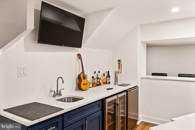 bar featuring hardwood / wood-style flooring, wine cooler, sink, light stone countertops, and blue cabinetry