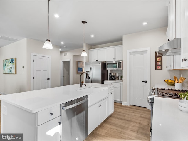 kitchen with an island with sink, light wood-type flooring, hanging light fixtures, white cabinetry, and appliances with stainless steel finishes