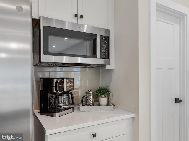 bar featuring decorative backsplash, stainless steel appliances, and white cabinets