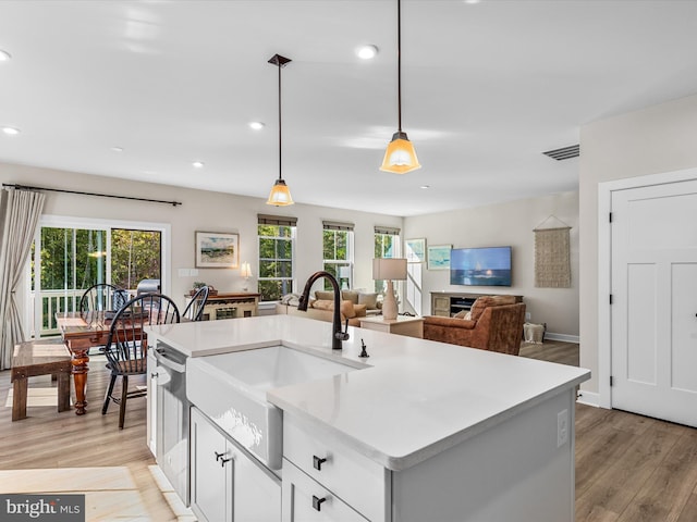 kitchen with white cabinets, sink, decorative light fixtures, a kitchen island with sink, and light wood-type flooring