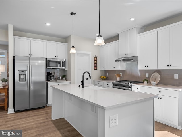 kitchen with tasteful backsplash, light hardwood / wood-style floors, pendant lighting, appliances with stainless steel finishes, and a center island with sink