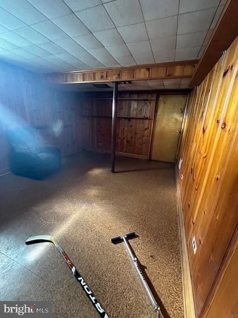 basement with a paneled ceiling and wooden walls