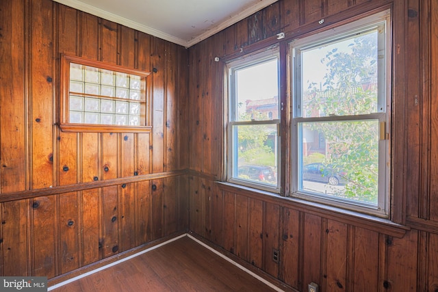 spare room featuring crown molding, dark hardwood / wood-style floors, wooden walls, and plenty of natural light