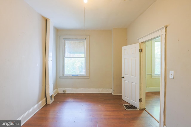 empty room with a wealth of natural light and dark hardwood / wood-style flooring