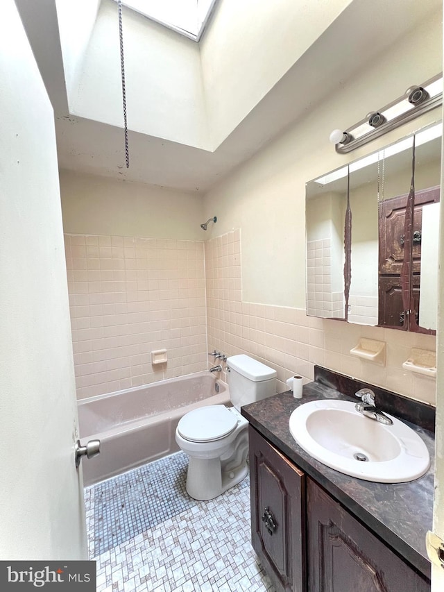 bathroom with tile patterned flooring, toilet, a skylight, vanity, and tile walls