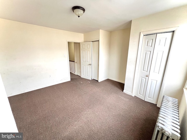 unfurnished bedroom featuring radiator heating unit, dark carpet, two closets, and baseboards