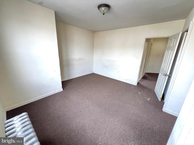 unfurnished room with baseboards and dark colored carpet