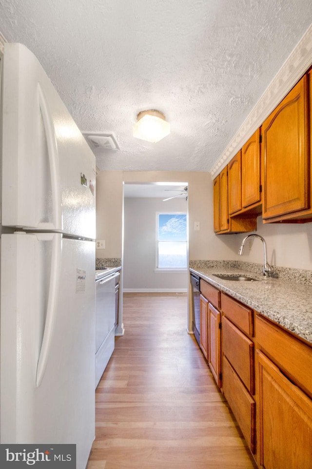 kitchen featuring light stone counters, a textured ceiling, sink, white appliances, and light hardwood / wood-style flooring