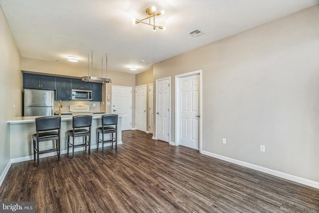 kitchen with kitchen peninsula, a chandelier, stainless steel appliances, dark hardwood / wood-style floors, and a kitchen breakfast bar