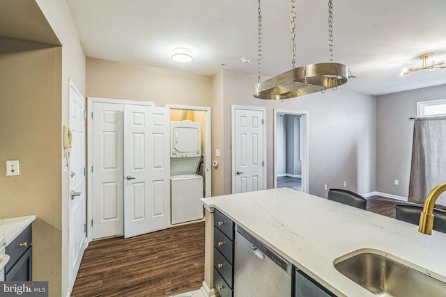 kitchen featuring dark wood-type flooring, stacked washer / dryer, sink, dishwasher, and light stone countertops