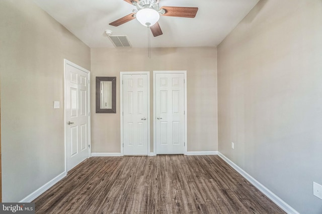 unfurnished bedroom featuring dark hardwood / wood-style floors, multiple closets, and ceiling fan