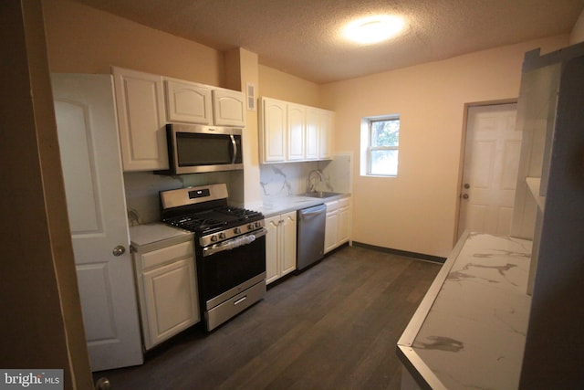 kitchen featuring sink, a textured ceiling, white cabinetry, stainless steel appliances, and dark hardwood / wood-style floors