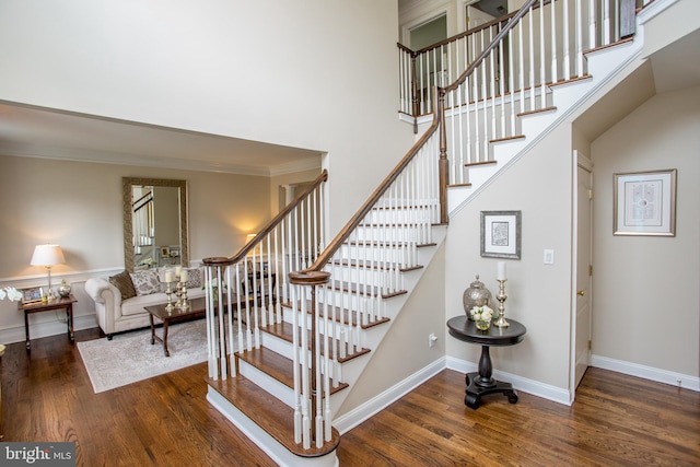 staircase featuring hardwood / wood-style flooring, crown molding, and a high ceiling