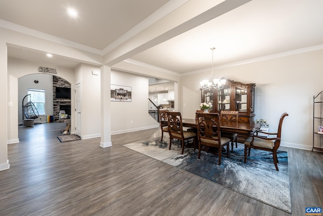 dining space featuring ornamental molding, a notable chandelier, dark wood-type flooring, and a stone fireplace