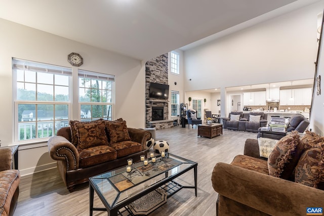 living room with light hardwood / wood-style flooring, a towering ceiling, and a stone fireplace