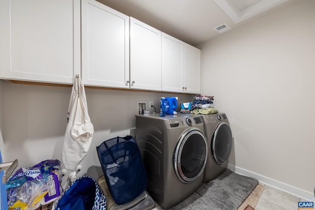 clothes washing area with washer and clothes dryer, light tile patterned floors, and cabinets